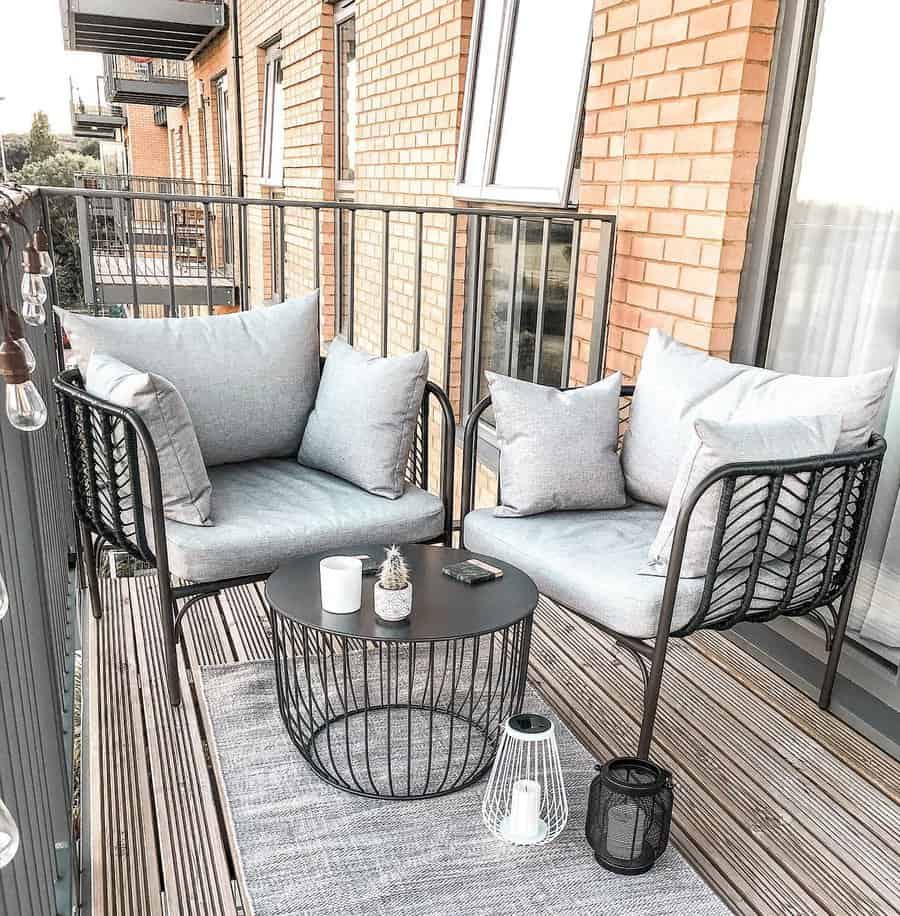 A cozy balcony with a seating area, featuring two gray cushioned chairs and a round black table with decor items on a rug