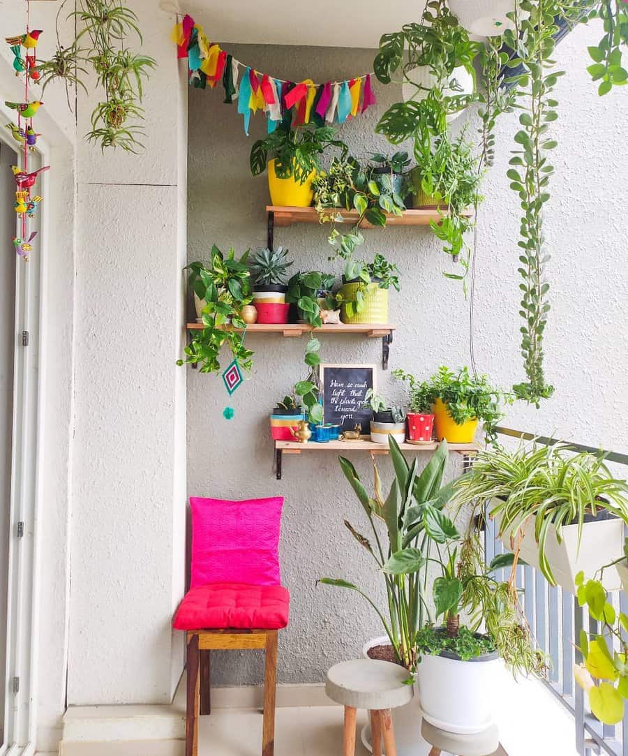 Lush balcony with floating plant shelves, colorful pots, hanging greenery, a bright pink cushion, and festive garland decor