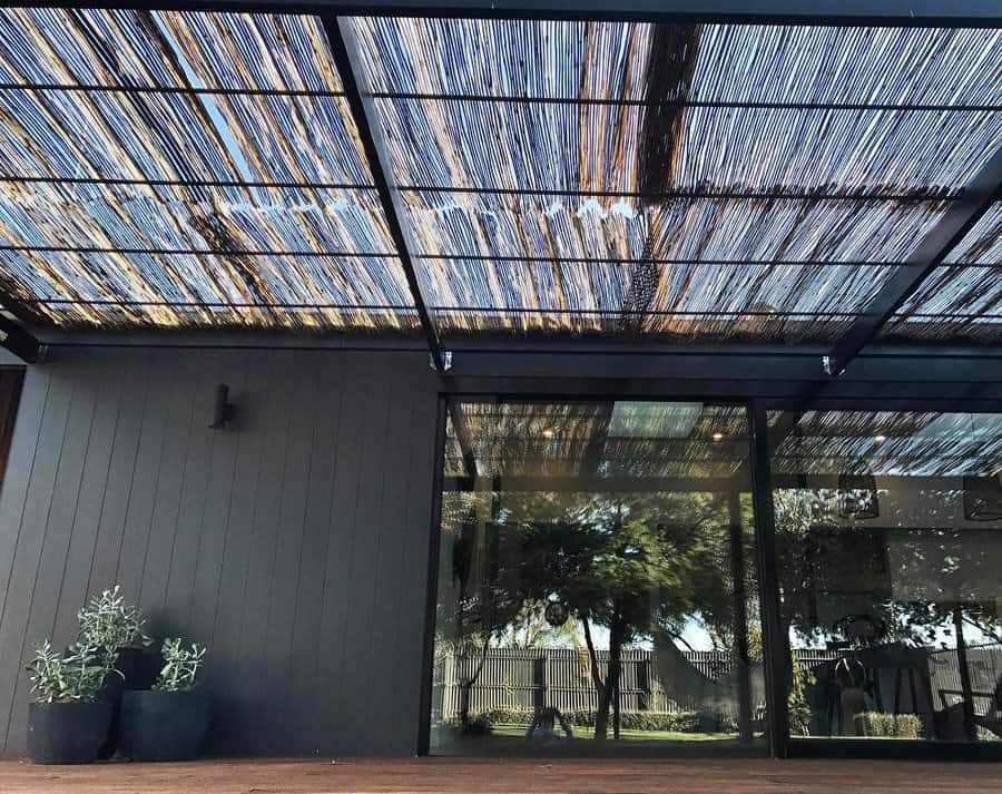 Patio with a slatted bamboo roof casting shadows; potted plants and glass doors leading to an interior space