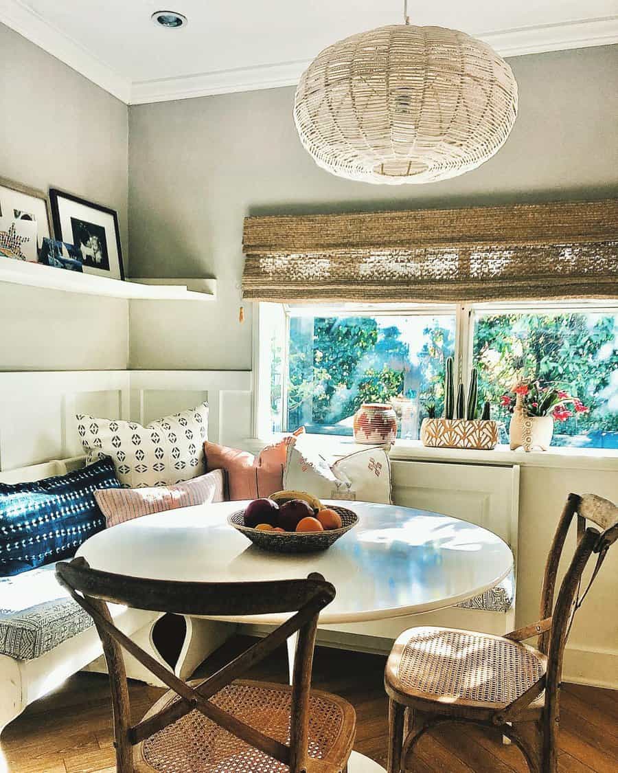 Cozy dining nook with a round white table, wicker chairs, cushions, and a pendant lamp