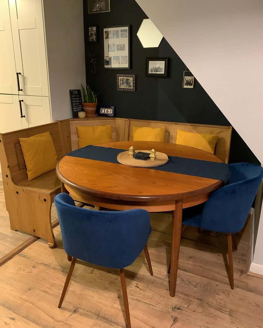 Cozy dining nook with a wooden table, built-in bench seating with yellow cushions, and blue chairs, under a black and white gallery wall