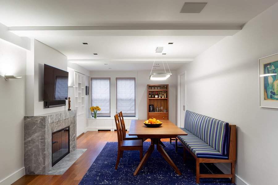 Modern dining room with a wooden table, striped cushioned seating, a TV above a fireplace, and a shelf in the background