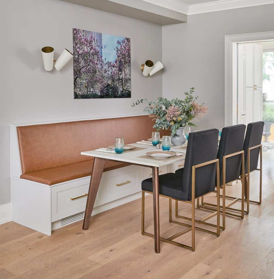 Modern dining room with a wooden table, black chairs, and a brown bench, featuring a floral arrangement and colorful artwork on gray walls