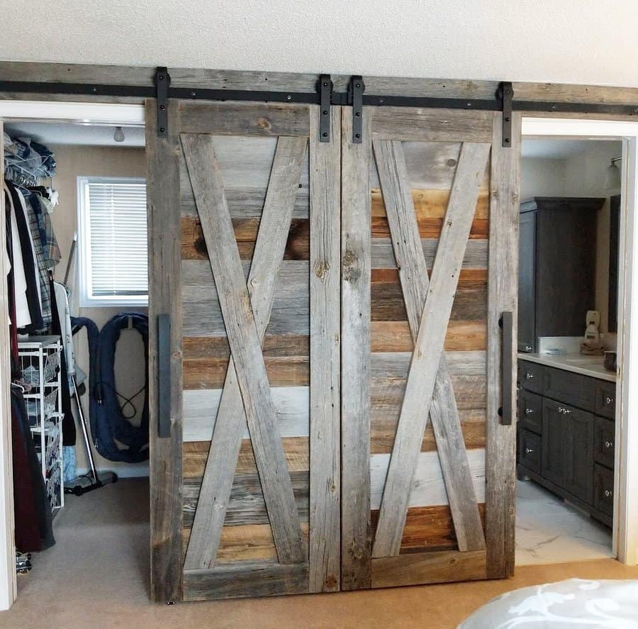 Rustic sliding barn doors with a chevron pattern separate a closet and bathroom in a cozy bedroom setting