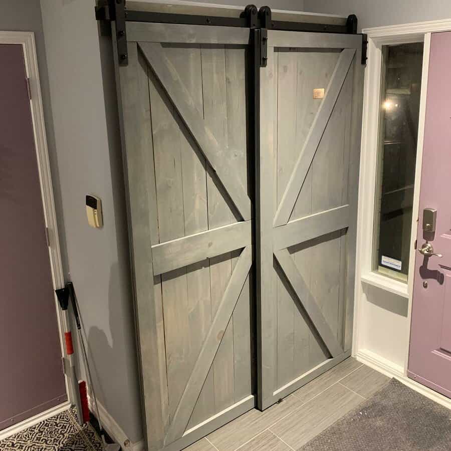 Grey wooden sliding barn doors in an interior room with a purple door and tiled floor