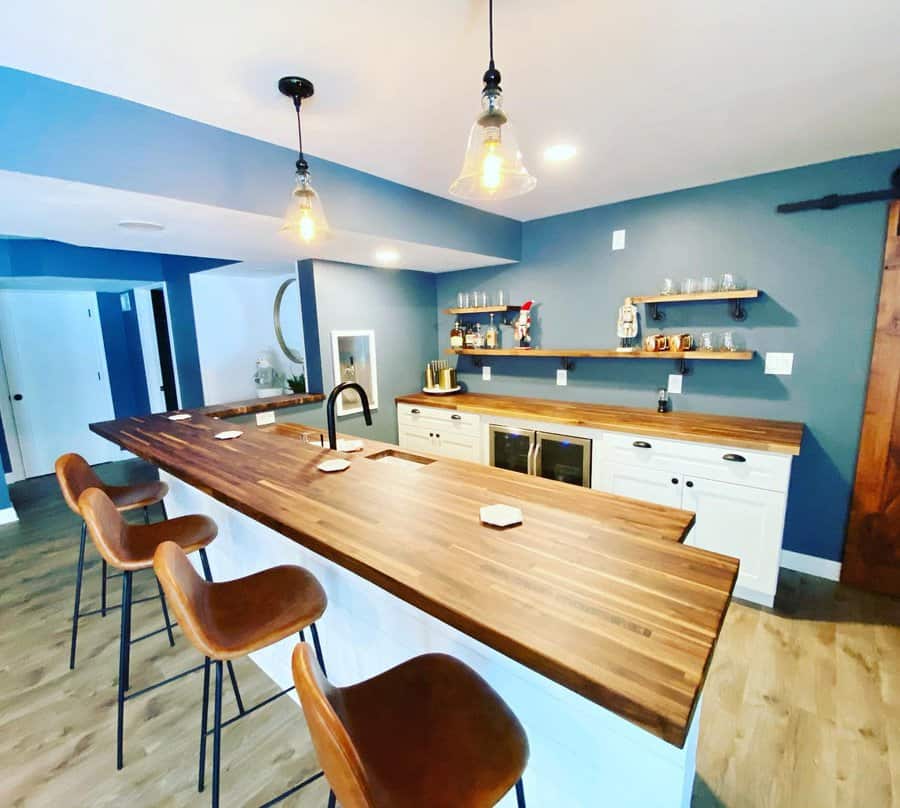 Warm and inviting basement bar with wood countertops, leather barstools, and navy blue walls for a stylish and functional space.