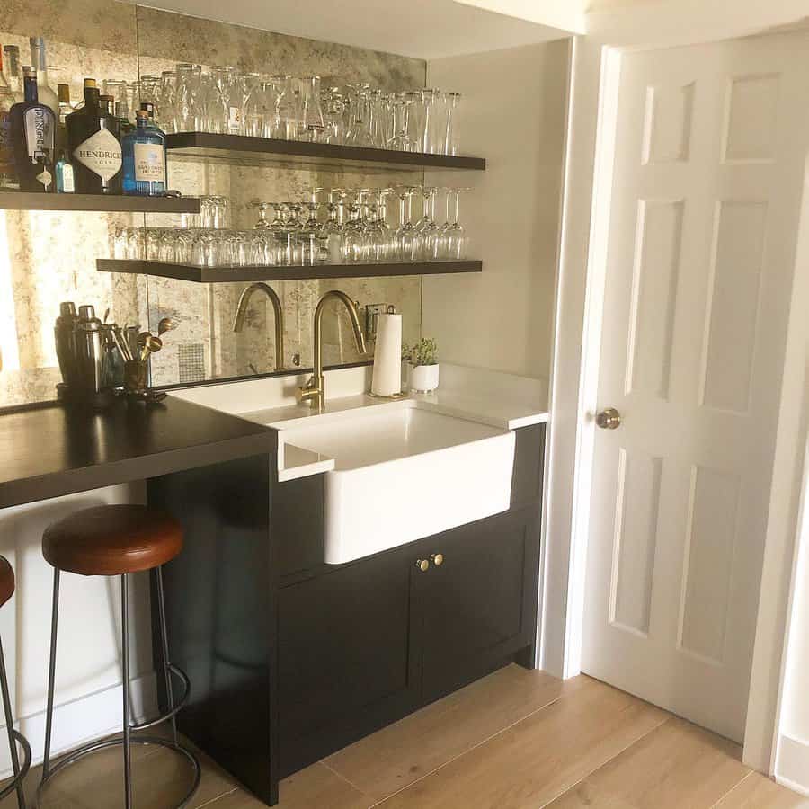 Stylish basement bar with a farmhouse sink, mirrored backsplash, black cabinetry, and open shelving for a sleek and functional space.