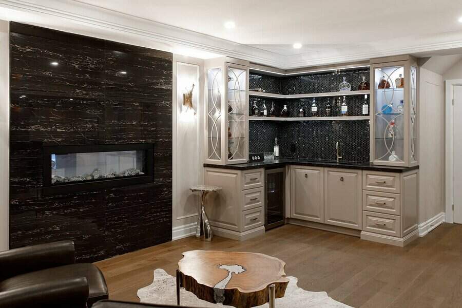 Elegant basement bar with glass cabinetry, dark mosaic backsplash, and built-in fireplace for a cozy yet sophisticated entertaining space.