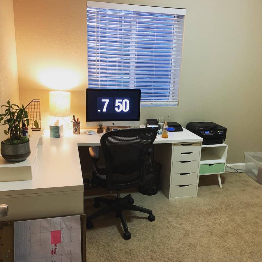 Cozy home office with an L-shaped white desk, ergonomic chair, warm lighting, and storage, creating a functional and inviting workspace