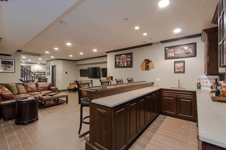 Spacious basement bar with dark wood cabinetry, counter space, leather sofas, sports decor on walls, and tile flooring