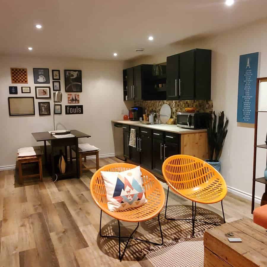 Warm basement open floor plan with a compact kitchen, eclectic decor, and vibrant orange chairs adding a playful touch