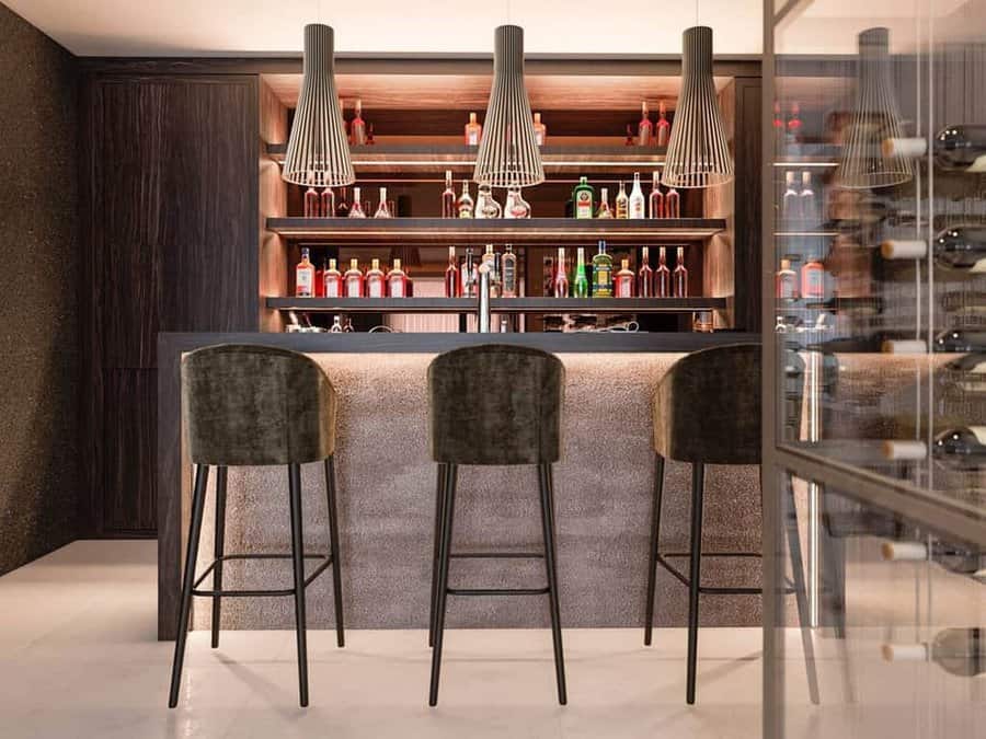 Contemporary home bar with built-in wine rack, wooden shelves displaying bottles, and three plush bar stools