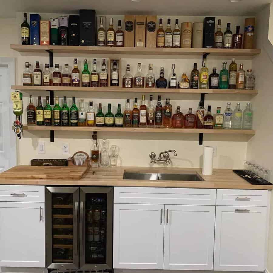 Home bar with open shelving displaying liquor bottles, white cabinetry, a wooden countertop, and a built-in wine fridge