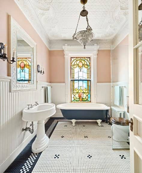 Elegant bathroom with an ornate white ceiling, vintage chandelier, and stained glass window, creating a classic and refined look.