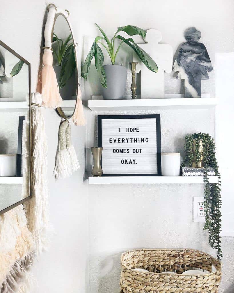 White floating shelves with greenery, candles, decorative figures, and a humorous letter board add a modern touch to this bathroom