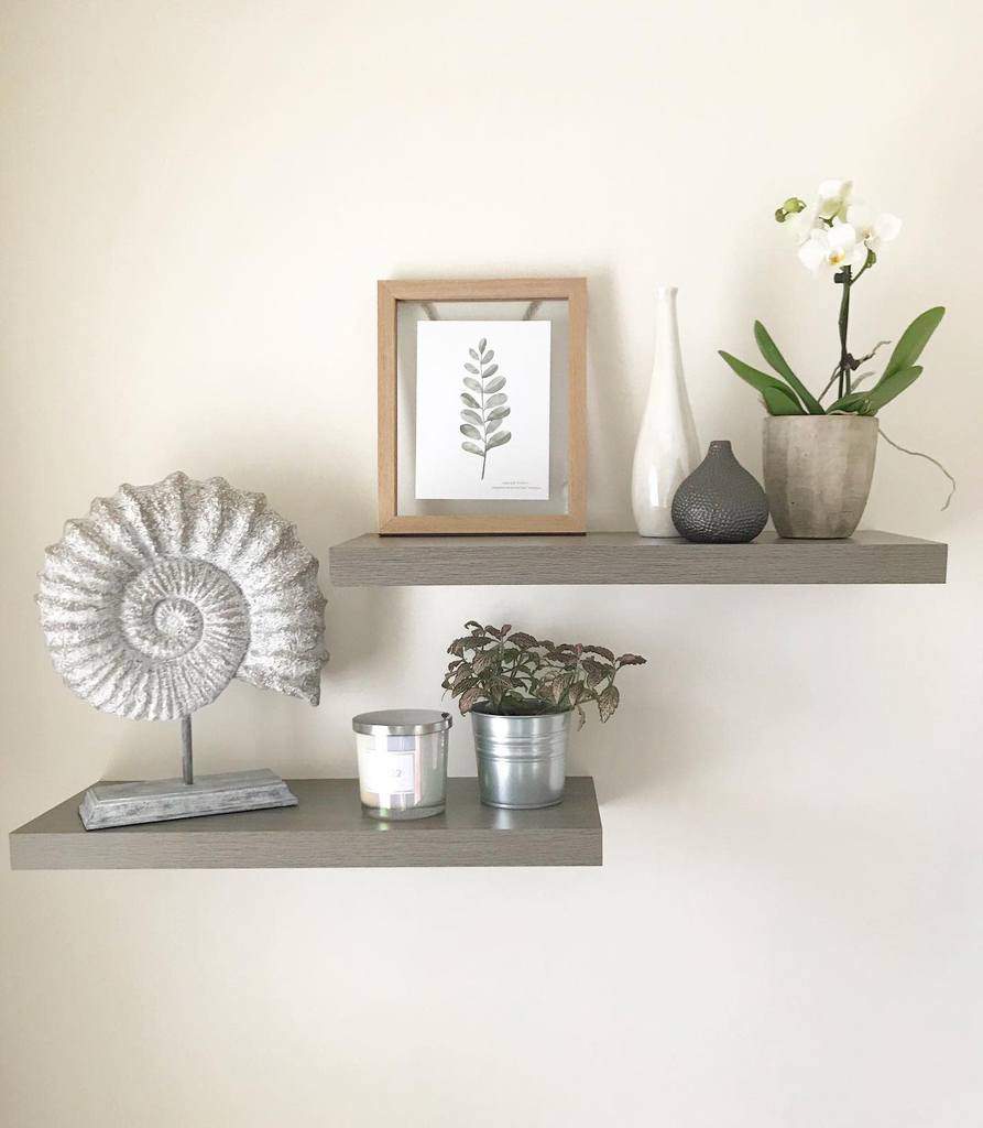 Two floating shelves with decor: framed leaf print, white geometric vase, orchid, ammonite sculpture, plant, candle