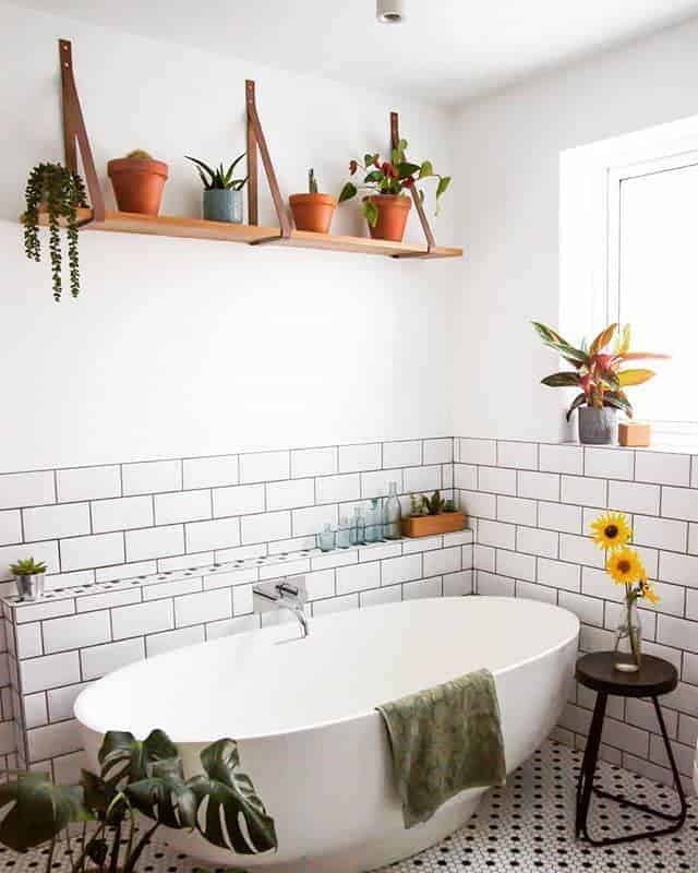 Wood and leather strap floating shelves with potted plants add a natural touch above a freestanding bathtub in a modern bathroom