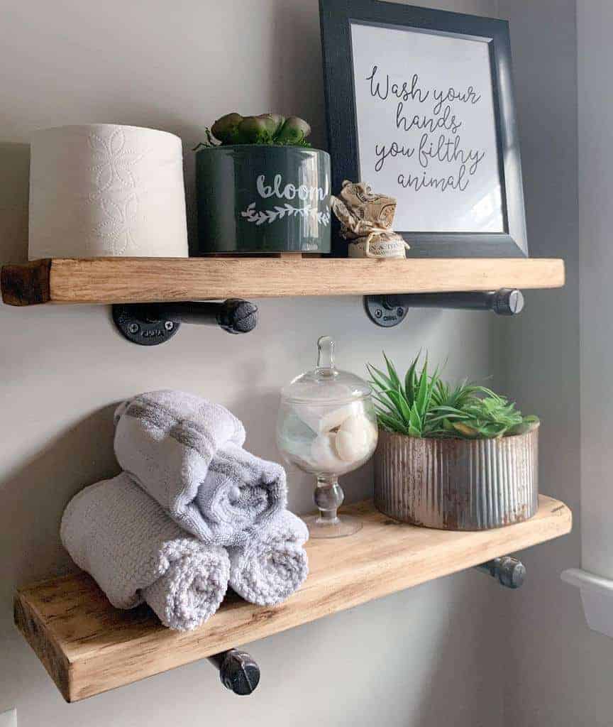 Bathroom shelves with decor: potted plants, towels, seashell jar, a framed sign reading "Wash your hands, you filthy animal," and a toilet roll