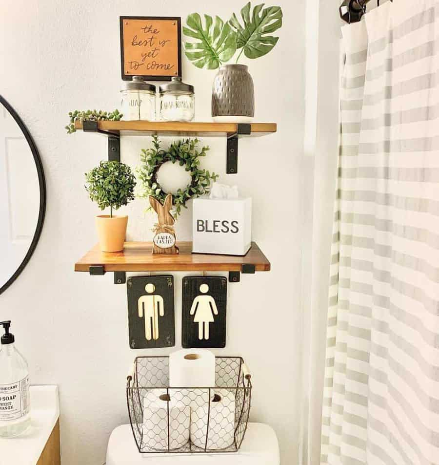 Rustic floating shelves above a toilet decorated with greenery, jars, a 'Bless' box, and a wire basket for toilet paper storage