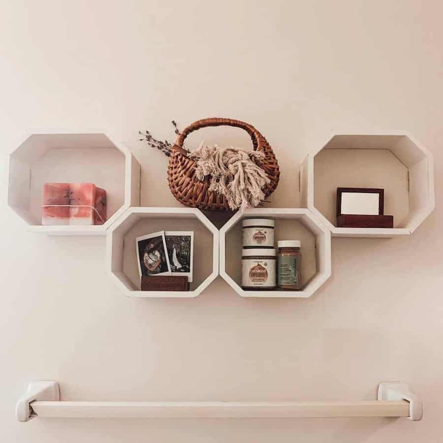 Hexagonal shelves with decor items: basket, candles, jars, and framed photos; wall-mounted above a towel bar; neutral wall color