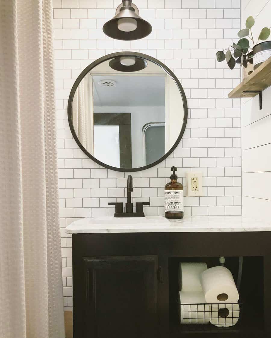 A minimalist RV bathroom with black cabinetry, white subway tiles, a round mirror, and practical storage for toiletries.