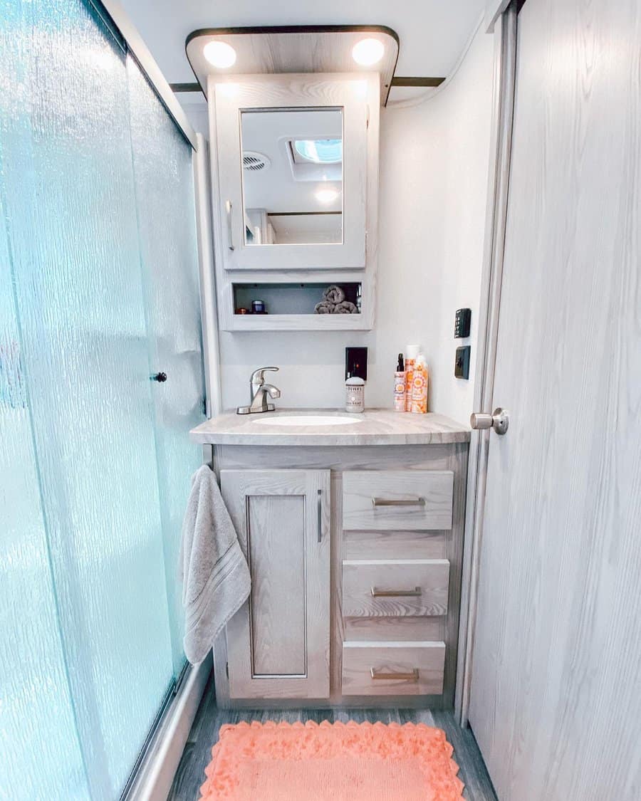 Bright RV bathroom with a vanity cabinet, mirrored storage, and open shelving, offering a stylish and functional space-saving solution.