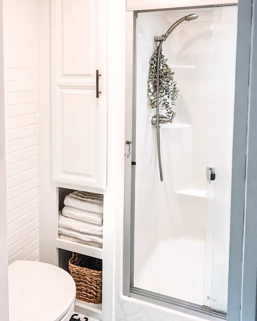 Minimalist RV bathroom with built-in towel shelves, a storage cabinet, and a glass shower door, maximizing space with smart organization.