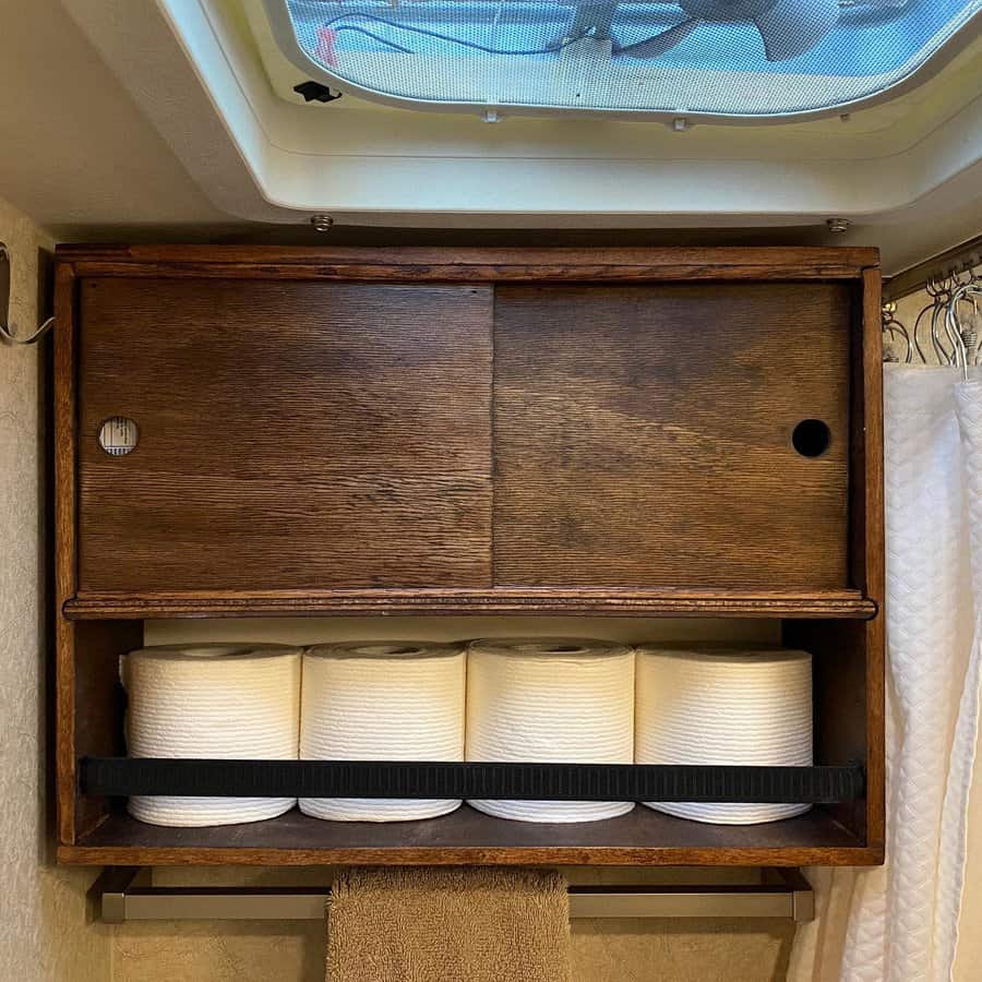 Wooden RV bathroom storage with sliding doors and a built-in shelf for toilet paper, maximizing space with a simple, rustic design.