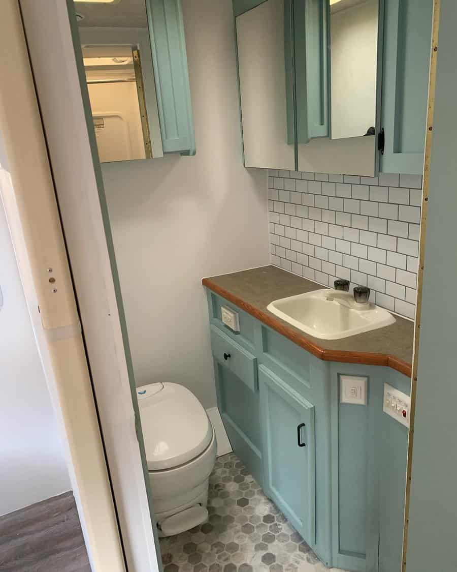 RV bathroom with pastel blue cabinets, a subway tile backsplash, and mirrored storage, creating a fresh and functional space.