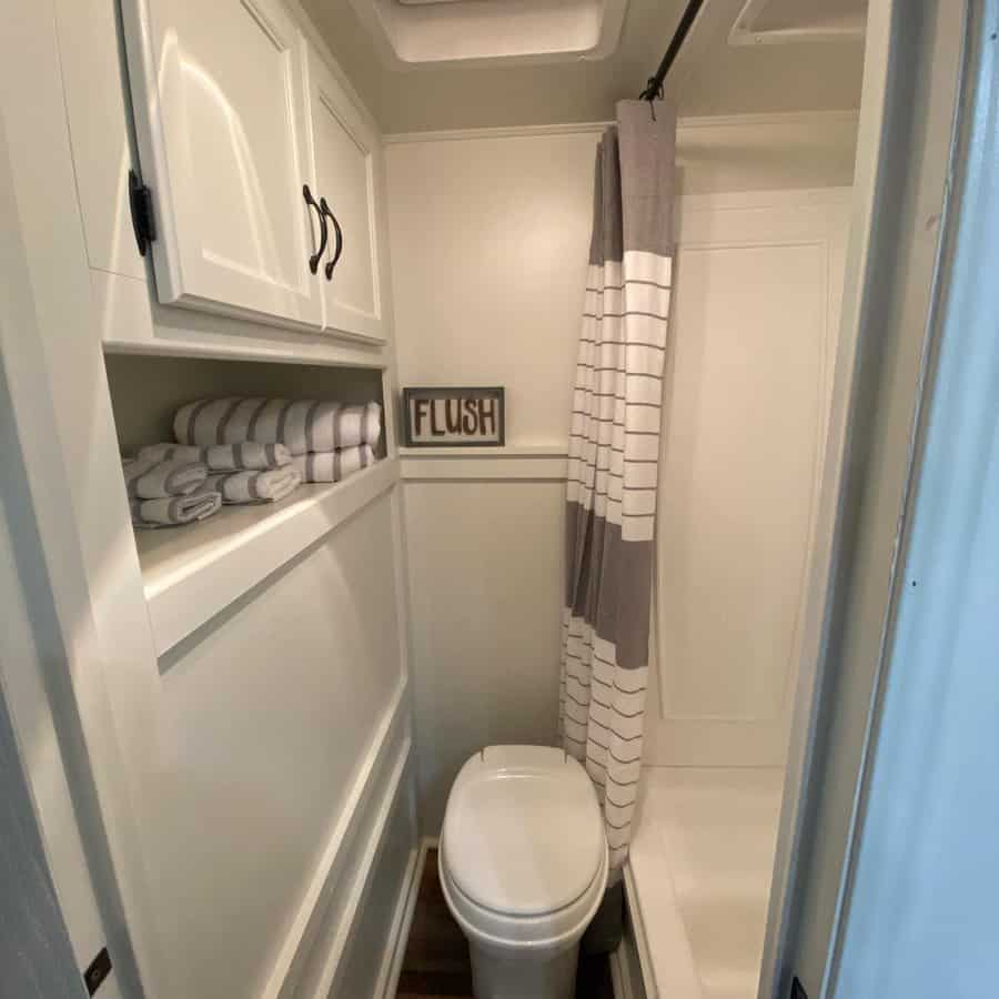 Compact RV bathroom with white cabinetry, built-in towel storage, and a striped shower curtain, creating a clean and organized space.