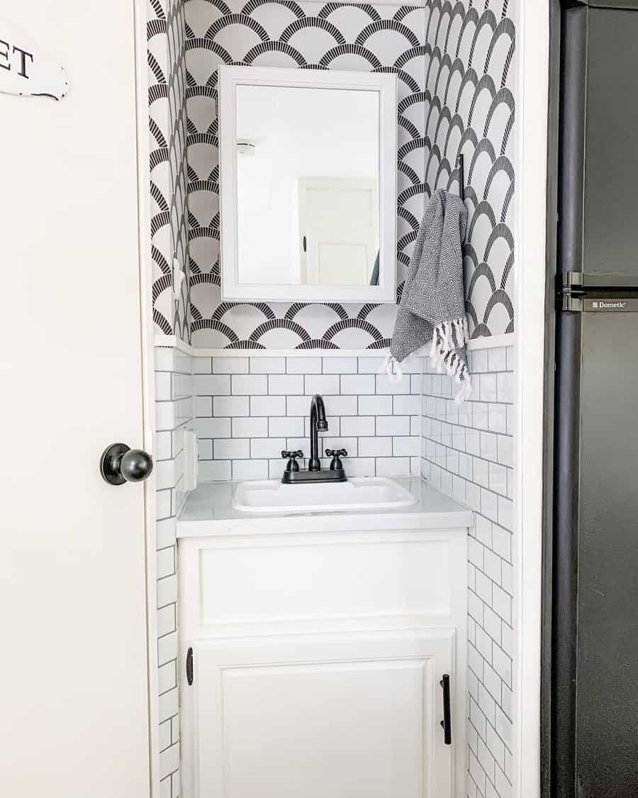 Small RV bathroom with white cabinetry, black-and-white patterned wallpaper, and a compact sink, blending style with space-saving storage.