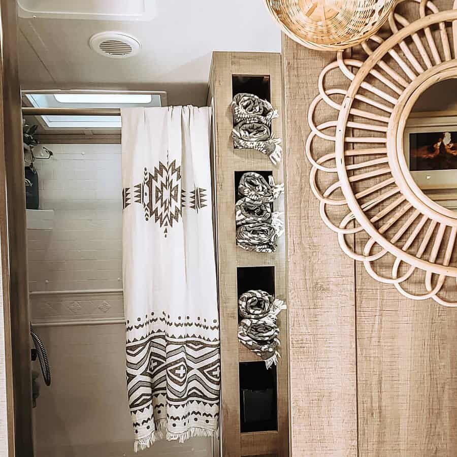 Boho-style RV bathroom with built-in towel storage, a geometric shower curtain, and a woven mirror, blending function with rustic charm.