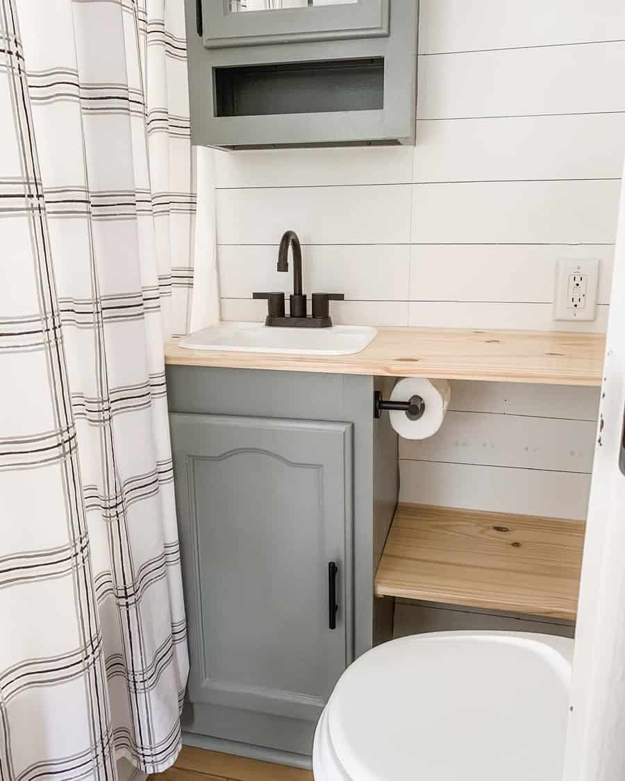 RV bathroom with gray cabinetry, a wood countertop, built-in storage, and a plaid shower curtain, combining function with farmhouse charm.