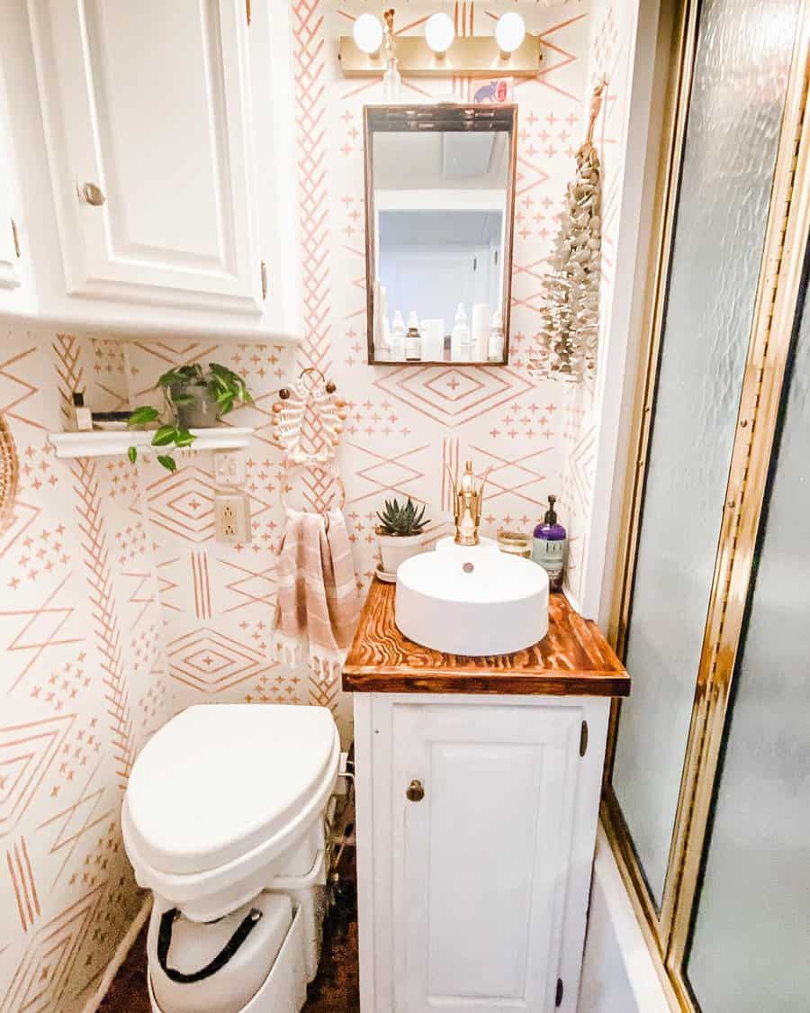 Boho-style RV bathroom with patterned wallpaper, white cabinetry, a wood countertop, and a vessel sink, creating a warm and stylish space.