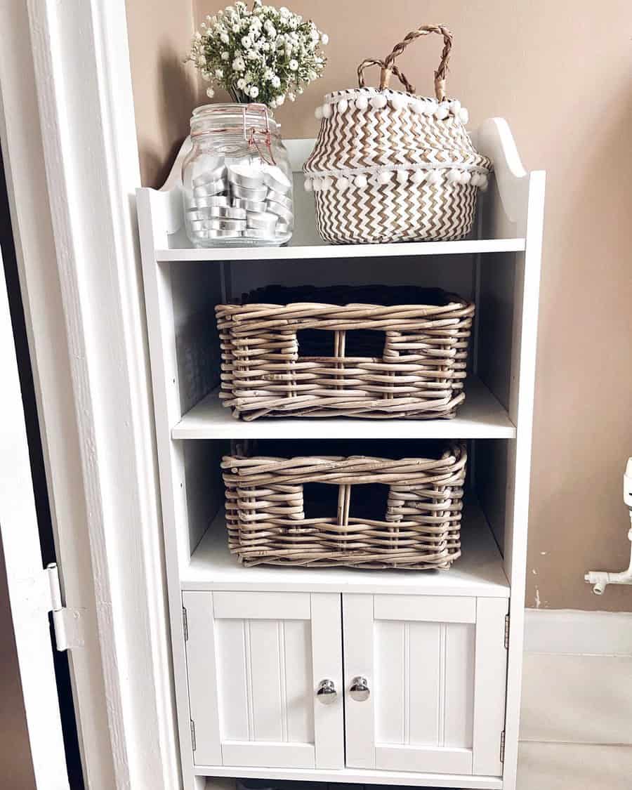 White cabinet with woven baskets, a glass jar containing spools of thread, and a potted plant on top against a beige wall