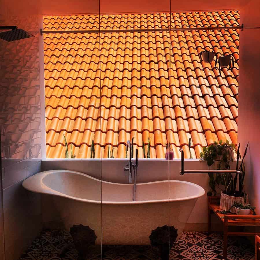 Elegant clawfoot bathtub in a glass-enclosed space with a view of terracotta roof tiles, blending rustic charm with modern luxury