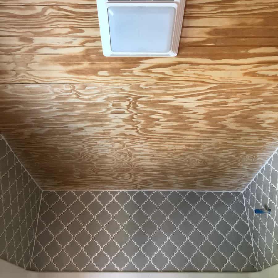 Bathroom with a natural wood ceiling and patterned tile walls, creating a warm contrast between rustic textures and modern design.