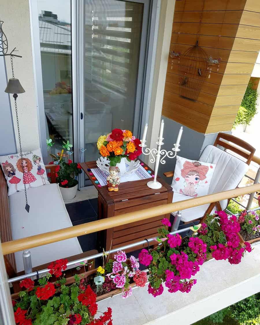 Small balcony with colorful flowers, a small wooden table, chairs with floral cushions, and a decorative candle holder