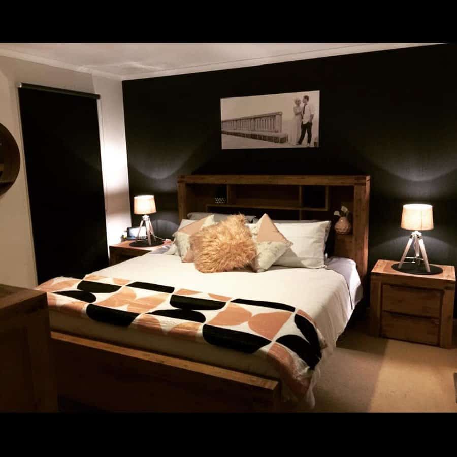 Cozy bedroom with a wooden bed frame featuring built-in book storage, warm lighting, decorative pillows, and a modern geometric blanket.