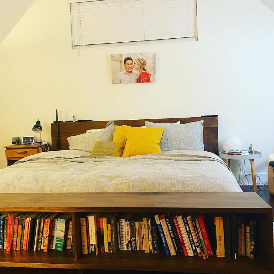 Cozy bedroom with a wooden bed frame featuring built-in bookshelf storage at the foot of the bed, neatly filled with colorful books.