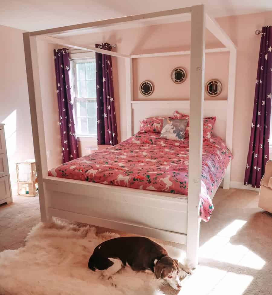 Canopy bed for kids with pink sheets and a dog lying on a shag rug