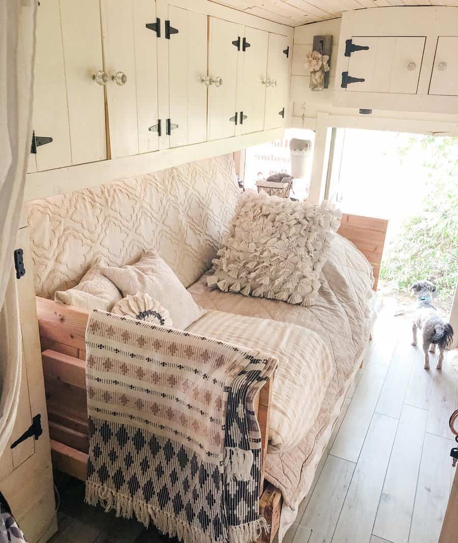 Cozy RV bedroom with built-in overhead cabinets, soft neutral bedding, and decorative pillows, blending storage with a rustic charm.