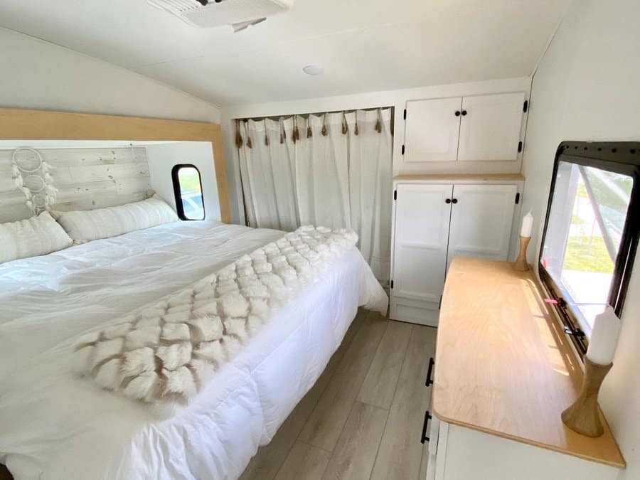 Minimalist RV bedroom with white cabinetry, a cozy bed with plush bedding, and natural wood accents, creating a bright and airy space.