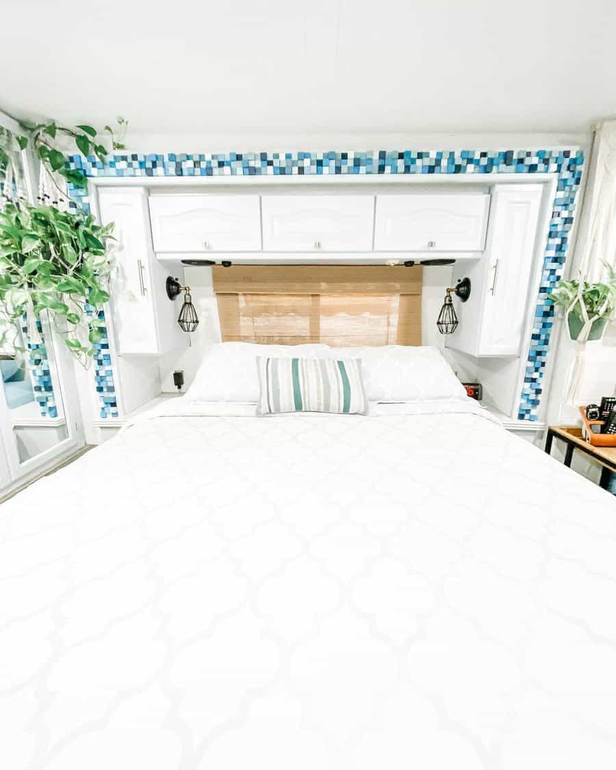 Bright RV bedroom with white cabinetry, blue mosaic tile accents, hanging lights, and greenery, creating a fresh and airy space.