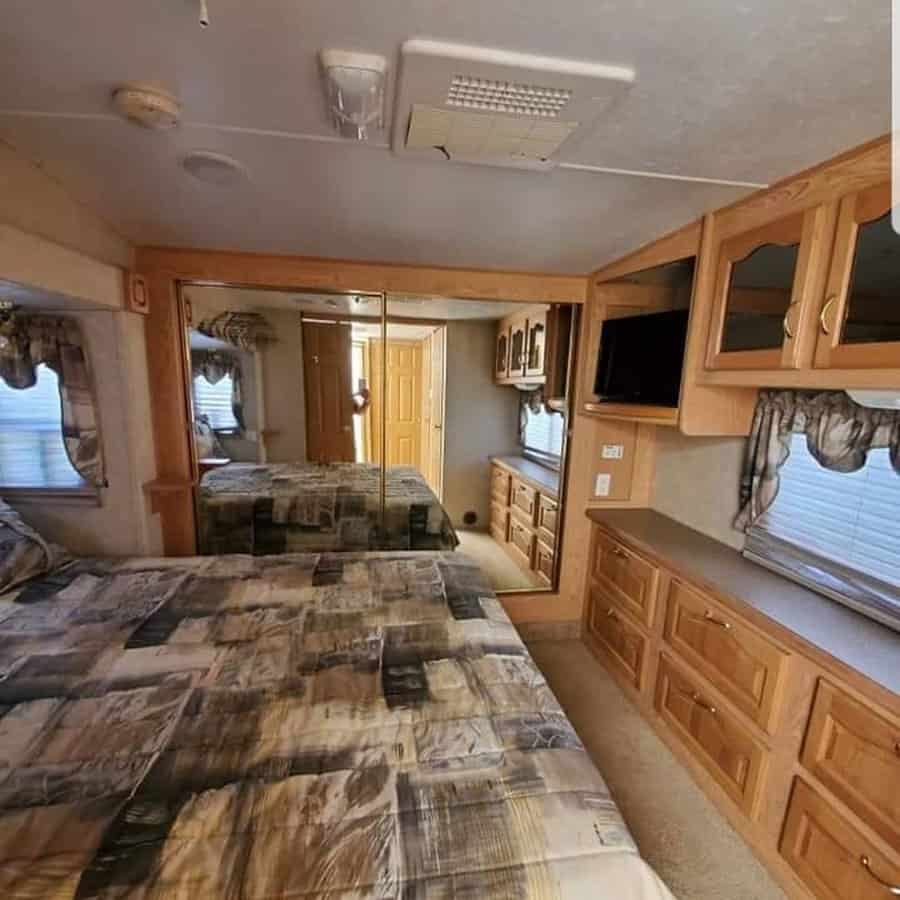 Spacious RV bedroom with wood cabinetry, mirrored closet doors, built-in storage, and a cozy bed, combining function with classic design.