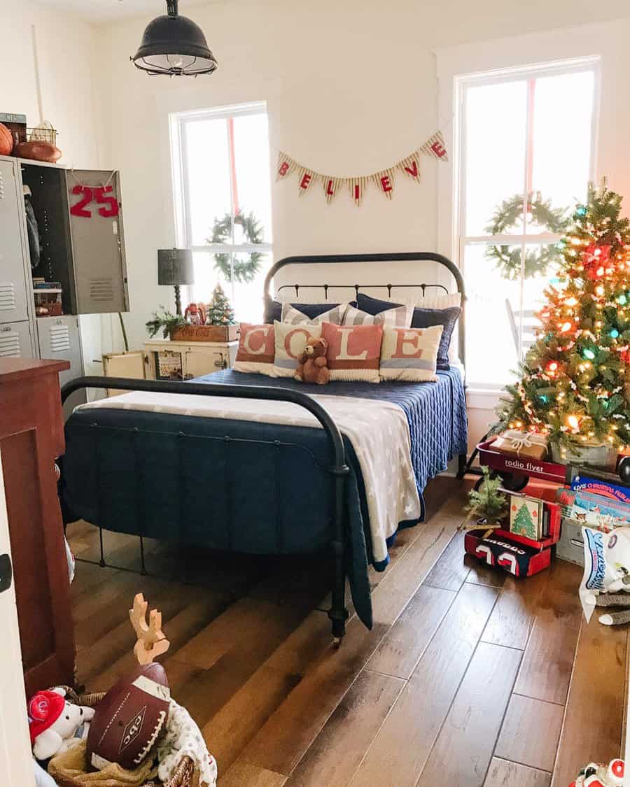 Festive bedroom with a metal bed, Christmas decorations, a "Believe" banner, wreaths, and a small Christmas tree with colorful lights