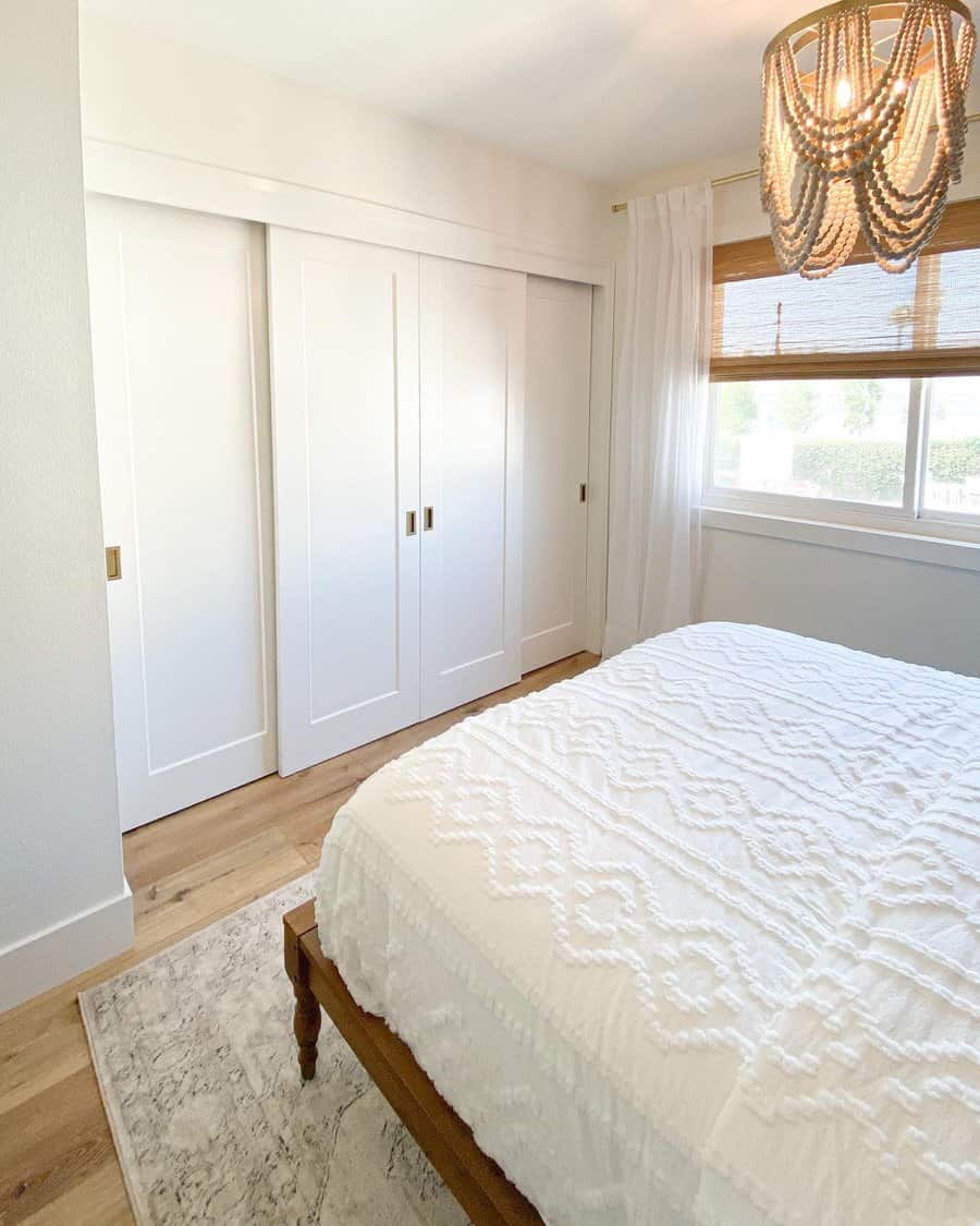 Simple white sliding closet doors with gold handles blend seamlessly into a cozy farmhouse-style bedroom with warm wood flooring and soft lighting