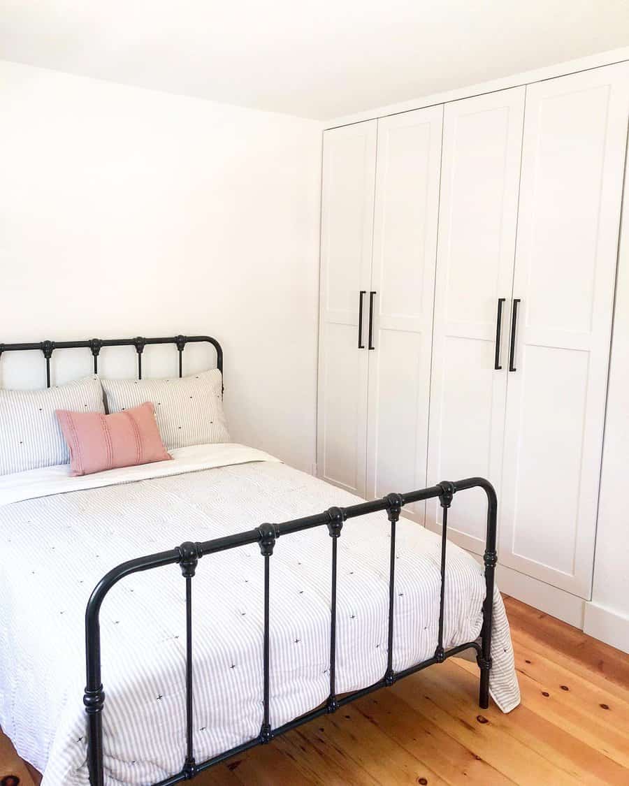 White shaker-style closet doors with black handles bring a sleek, modern touch to a cozy bedroom with a vintage black metal bed frame and wood flooring