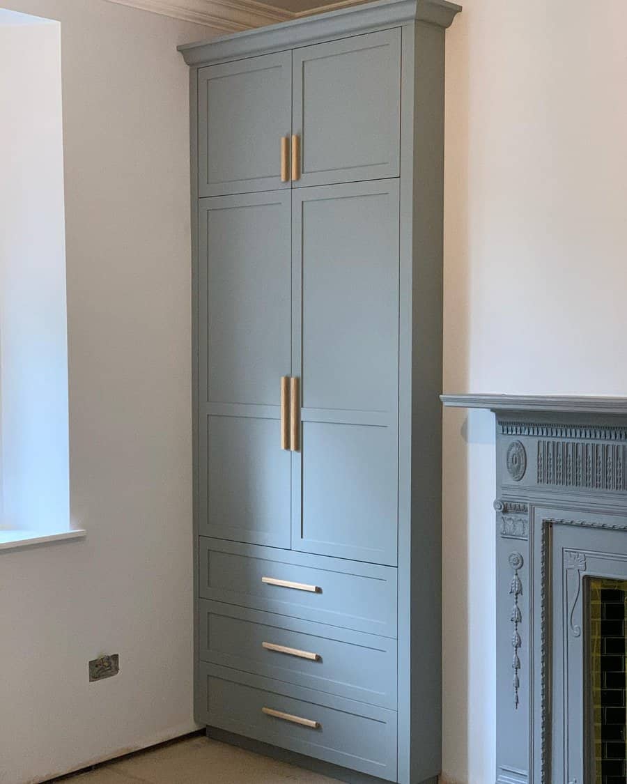 Tall grey cabinet with gold handles beside a decorative fireplace in a room with light walls