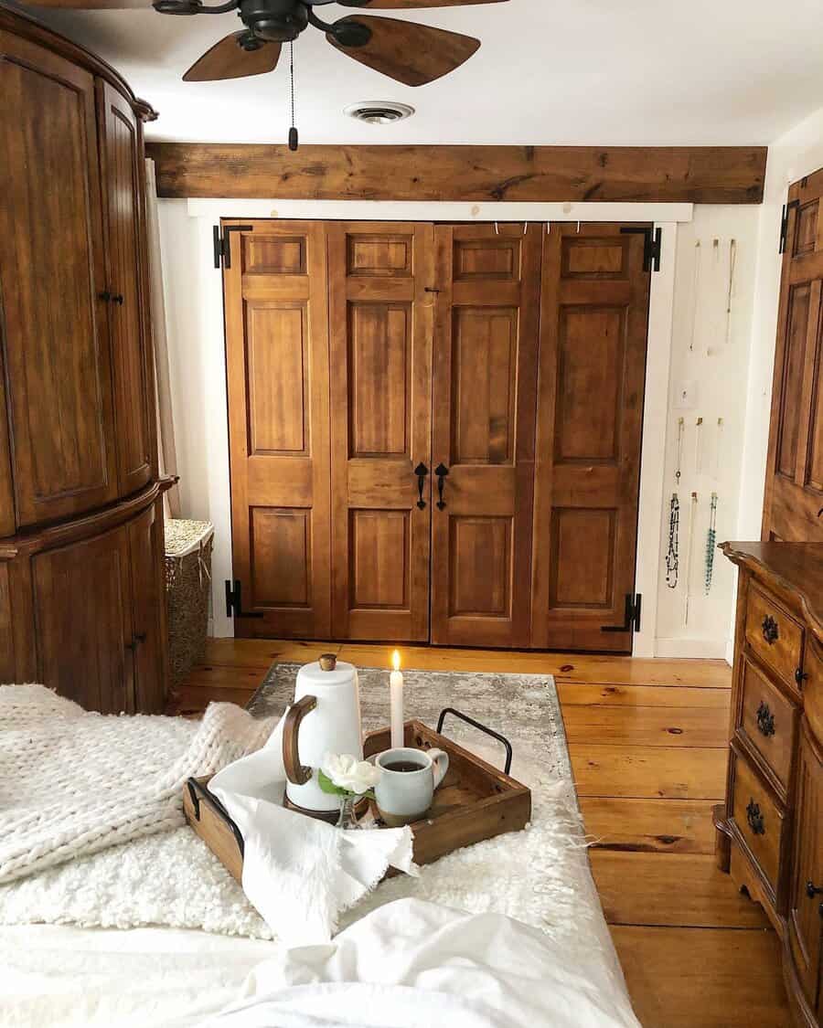 Rich wooden barn-style closet doors with black hardware bring a rustic charm to this cozy bedroom with warm wood tones and vintage decor